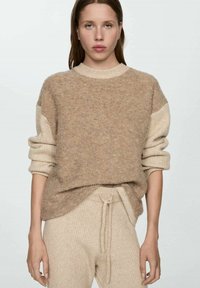 Beiger Strickpullover mit langen Ärmeln, lockerer Passform und gerippten Akzenten an den Bündchen. Kombiniert mit passenden, gerippten beigen Hosen.
