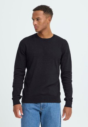 Black knitted sweater with long sleeves, crew neckline, and ribbed cuffs. Paired with light blue denim jeans. Smooth texture.