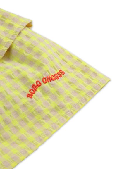 Yellow and beige checked fabric with a textured surface. Features embroidered red text "ROBO CHOSES" near the edge.