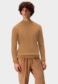 Beige gerippter Strickpullover mit hohem Kragen und langen Ärmeln, kombiniert mit strukturierten Cordhosen in einem ähnlichen Farbton.