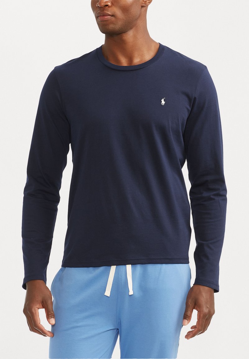 Navy long-sleeve cotton shirt with a crew neck and logo detail. Soft texture, fitted design, paired with light blue pants.