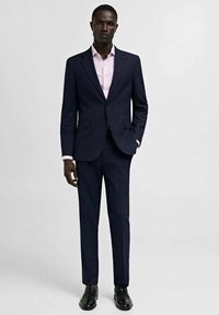 Marineblauw op maat gemaakt pak met een notch revers, gecombineerd met een lichtroze overhemden. Zwarte dresschoenen maken de look compleet. Vriendelijke stoftextuur.