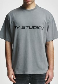 Hallide hallide t-särk, lühikeste varrukatega, millel on rindkeres julge must kiri "2Y STUDIOS". Laisk lõige ja sile tekstuur.