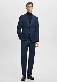 Granatowy garnitur z usztywnioną marynarką i dopasowanymi spodniami, uzupełniony czarnym golfem. Gładka tkanina bez widocznych wzorów czy ozdób.
