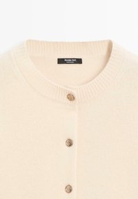 Cardigan beige con scollatura a costine, dotato di chiusura a bottoni in metallo dorato. Tessuto a maglia morbido e design semplice.