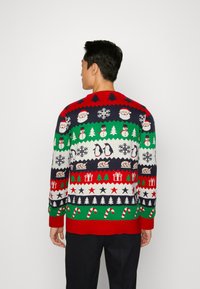 Kötött ünnepi pulóver piros, zöld és tengerészkék színben, amelyen Mikulás, pingvinek, hópelyhek és fák láthatók ismétlődő mintában. A pulóver bordázott mandzsettával és aljjal rendelkezik.