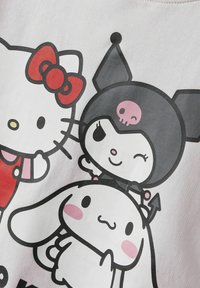 T-shirt di colore grigio chiaro con una stampa grafica che presenta i personaggi: Hello Kitty con un fiocco rosso, un personaggio nero con un teschio e un coniglio bianco.