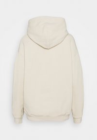 Sudadera beige de gran tamaño con una textura suave, capucha grande y puños y dobladillo acanalados. Presenta un diseño minimalista sin marca visible.