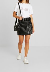 Černá mini sukně z umělé kůže s předním zipem, ve spojení s bílým tričkem s grafickým potiskem a bílými teniskami. Obsahuje černou kabelku přes rameno.