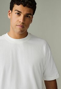 Hvid bomulds T-shirt med rund hals, korte ærmer og løs pasform. Glat tekstur med minimal syning og uden synlige mønstre.