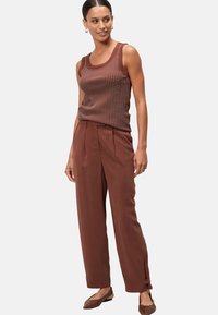 Top sans manches marron avec un motif à pois, associé à un pantalon marron taille haute avec des plis et des liens aux chevilles. La mannequin se tient avec assurance.