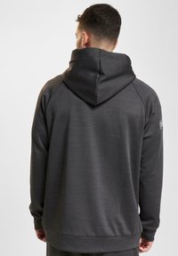 Felpa grigia scura con cappuccio ampio, maniche lunghe e orlo a coste. Presenta una texture liscia e dettagli di cucitura discreti.