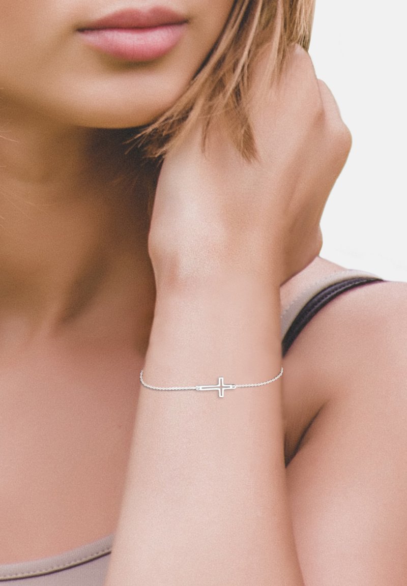 Bracciale in argento con ciondolo a forma di croce, mostrato su un polso di tonalità della pelle. Il bracciale ha un design delicato e accenti minimalisti.