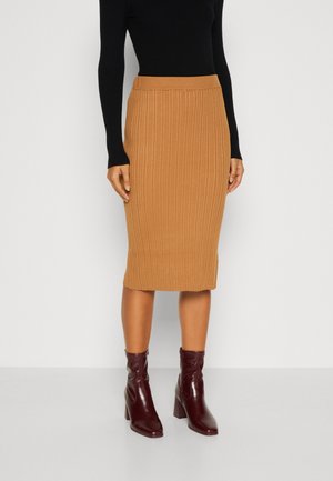 Jupe crayon côtelée beige avec une taille haute, associée à un haut noir à manches longues et des bottines bordeaux. Texture lisse et forme ajustée.