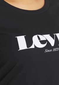 Camiseta de algodón negra con un gran logo blanco que presenta la palabra "Levi's" y el texto "Desde 1873", exhibiendo un cuello redondo y una textura suave.