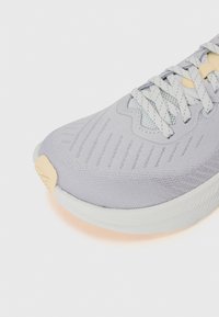 Light gray athletic shoe featuring a breathable mesh upper, textured accents, and a cushioned white sole with a rubber toe cap.