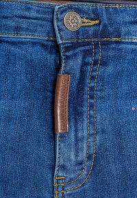 Jeans i mörkblå denim med synliga sömmar. Har en läderetikett med "GIANNI KAVANAGH" präglad och en metallknäppning.