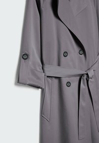 Grauer Trenchcoat mit doppelter Knopfleiste, schwarzen Knöpfen und einem selbst gebundenen Gürtel. Aus glattem, leichtem Stoff mit umgeschlagenen Ärmeln gefertigt.