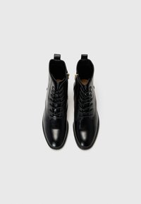 Black leather ankle boots with a smooth finish, featuring lace-up front, side zippers, and small pull tabs on the back.