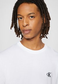 T-shirt bianca in cotone con collo a giro e un piccolo logo "cK" nero sul petto sinistro. Tessuto liscio con maniche corte.