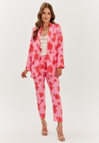 Růžový květinový oblek s červenými listovými vzory, obsahující sako a těsné kalhoty. Hladká tkanina se strukturovaným tvarem a rozšířenými rukávy.