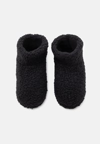 Črne flis copate z teksturirano, puhasto zunanjostjo, zaobljenim prstom in zasnovo do gležnja. Mehka, topla obloga za udobje.