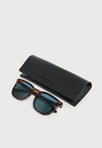 Occhiali da sole tartarugati con lenti azzurre accanto a una custodia nera con marchio. La montatura è rettangolare con una finitura lucida.