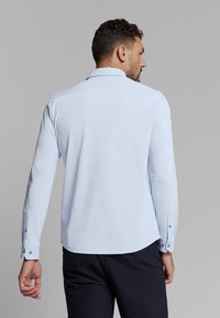Lichtblauw langemouwen shirt met een klassieke kraag, knoopmanchetten en een gladde textuur. De achterzijde toont een rechte snit en subtiele glans.