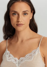 Camiseta ligera color beige con un delicado borde de encaje blanco en el escote, tirantes finos y una textura suave y lisa.