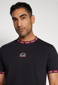 Black crew-neck t-shirt with red and blue logo detailing on collar and sleeves. Features a small embroidered logo on the chest.