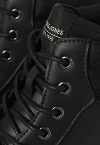 Baskets montantes noires en cuir et en mesh, dotées d'œillets en métal et de lacets noirs, avec une étiquette de marque affichant "Jack & Jones EST. 1990."