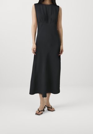 Czarna sukienka bez rękawów z dopasowanym gorsetem, rozkloszowaną spódnicą o długości midi i gładką fakturą; zestawiona z czarnymi sandałami na obcasie z paskami.