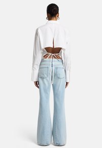Chemisier blanc court avec un dos ouvert et un détail à nouer, associé à un jean évasé bleu clair. Les deux pièces présentent des styles décontractés et amples.