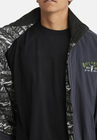 Billabong jacket with a dark blue exterior, patterned black and white lining, and black t-shirt underneath. Features a corduroy collar.