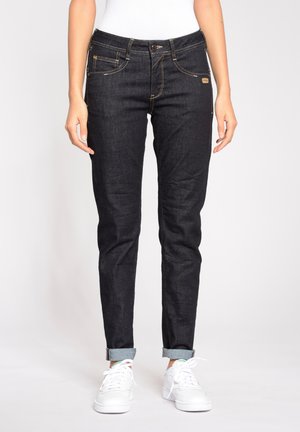 Dunkelblaue Jeans aus Denim mit einer figurbetonten Passform, Fünf-Taschen-Stil, gelben Nähten und umgeschlagenen Säumen. Kombiniert mit weißen Turnschuhen.