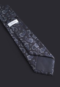 Seidene Krawatte in Marineblau mit weißem Blumen-Paisleymuster, spitzem Ende und einem angenähten Etikett "LES DEUX" am schmalen Ende, mit glatter Textur.