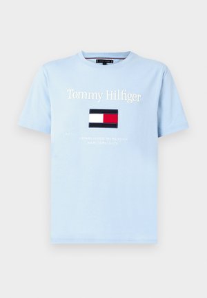Ljusblå t-shirt med korta ärmar som har "Tommy Hilfiger"-text och en rektangulär logotyp i röd, vit och marinblå färg på bröstet.