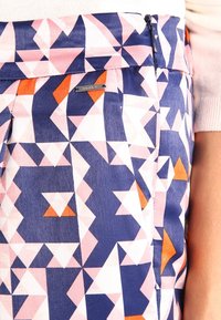 Pantalons à motifs dans un design géométrique comprenant des couleurs rose, marine et orange. Fabriqués en tissu lisse avec une étiquette de marque discrète et une fermeture éclair.