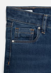 Tmavě modré džíny z denimu s designem pěti kapes, světlým prošitím, malou kapsičkou na mince a kovovým zapínáním na pasu.