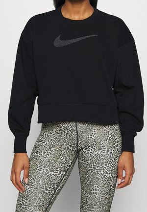Czarna, długorękawowa bluza Nike, połączona z legginsami w zwierzęcy wzór z wysokim stanem na stojącej osobie.