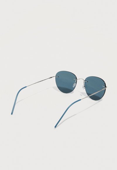 Lunettes de soleil sans monture en forme de papillon teintées de bleu, avec des branches fines en métal argenté et des embouts incurvés bleus, sur fond blanc.