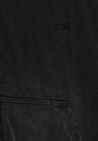 Tissu en denim noir avec une poche avant et un petit logo brodé indiquant "Swift" près du centre supérieur.