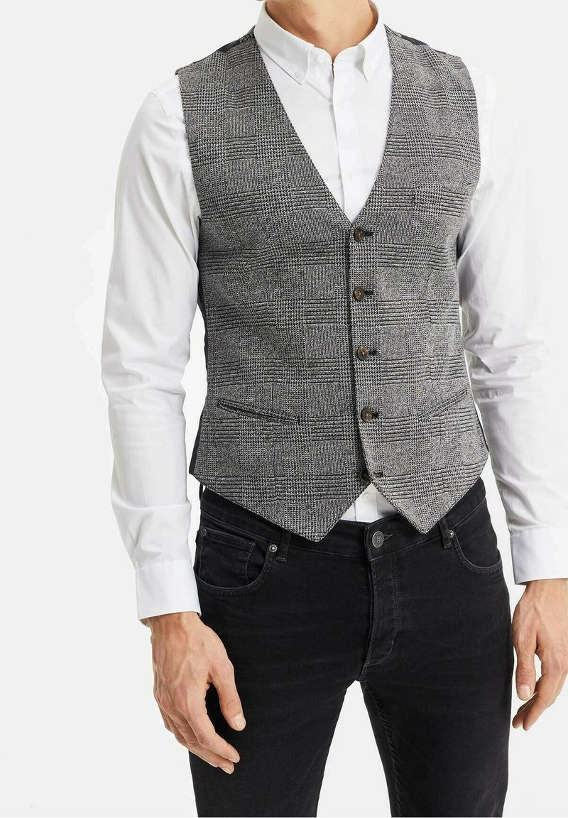 Grårutigt väst med V-hals, med sex knappar, som bärs över en vit skjorta. Tygtexturen är vävd, med en figurnära design och spetsig nederkant.
