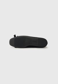 Chaussure noire plate avec une semelle en caoutchouc texturé, un matériau supérieur lisse et une languette à boucle à l'arrière pour un enfilage facile.