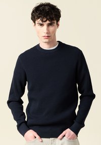 Marinblå stickad tröja med strukturerat mönster, ribbad rund halsringning och muddar. Slim fit-design med långa ärmar och en subtil finish.