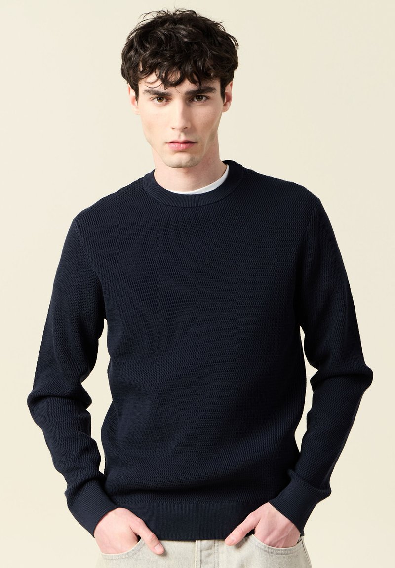 Marinblå stickad tröja med strukturerat mönster, ribbad rund halsringning och muddar. Slim fit-design med långa ärmar och en subtil finish.