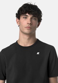 T-shirt nero a maniche corte realizzato in tessuto liscio, con un piccolo logo bianco nella parte sinistra del petto e un colletto rotondo.
