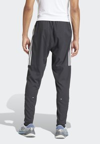 Schwarze Sporthose mit drei weißen vertikalen Streifen an den Seiten, elastischem Bund und schmal zulaufenden Beinen. Leichtes Material mit reflektierenden Akzenten.