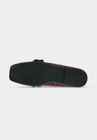 Semelle de chaussure avec une semelle en caoutchouc noire texturée, présentant un bout carré et une tige à carreaux multicolores visible de côté.