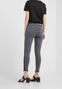 Jeans ajustados en denim gris oscuro con dobladillo sin terminar, diseño de cinco bolsillos y cinturilla con marca. Combinados con sandalias negras de tacón cuadrado.